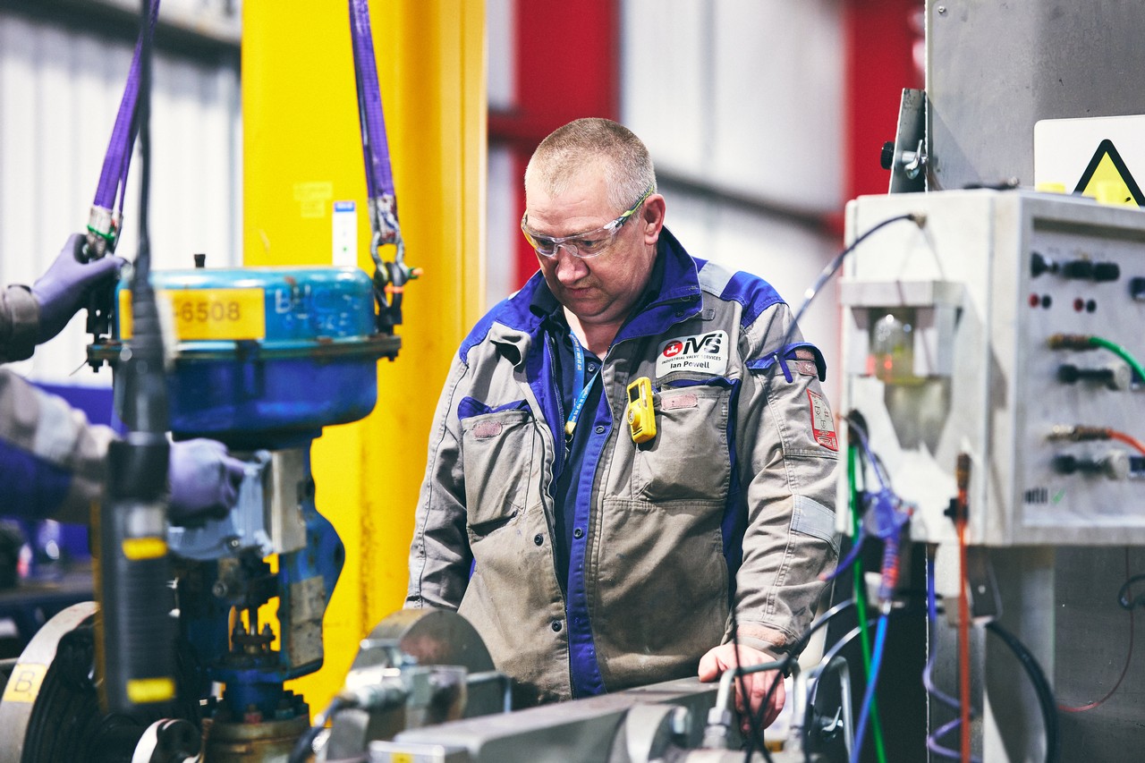 A technician from IVS examines equipment in an industrial workshop setting.