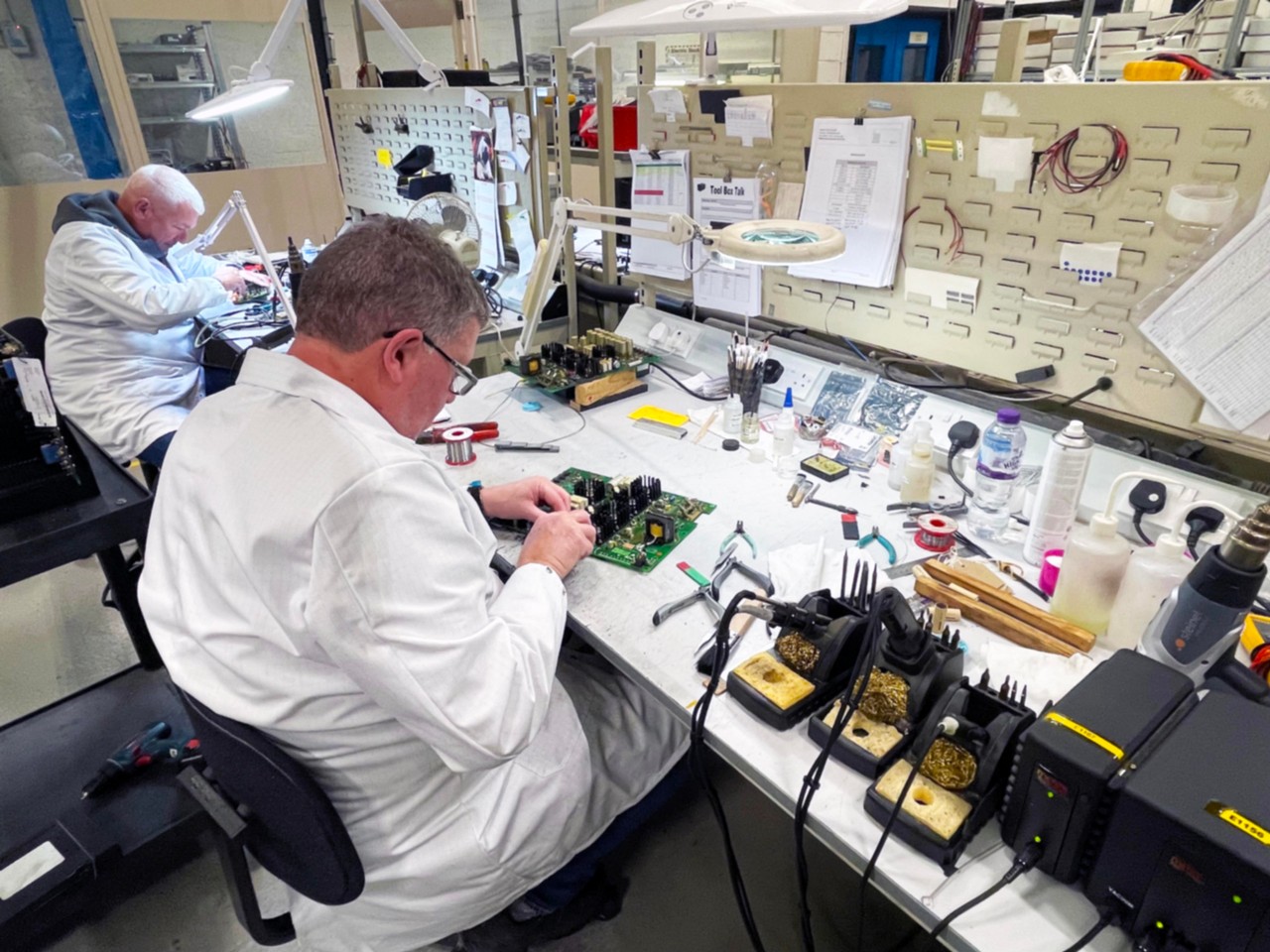 Technicians repairing and testing electronic equipment in a well-equipped workshop.