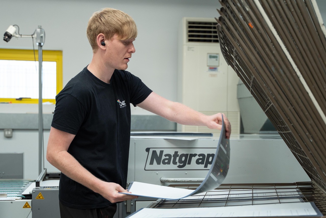 Bex Design & Print Limited - Bex specialist examining a piece of print equipment in a workshop setting.