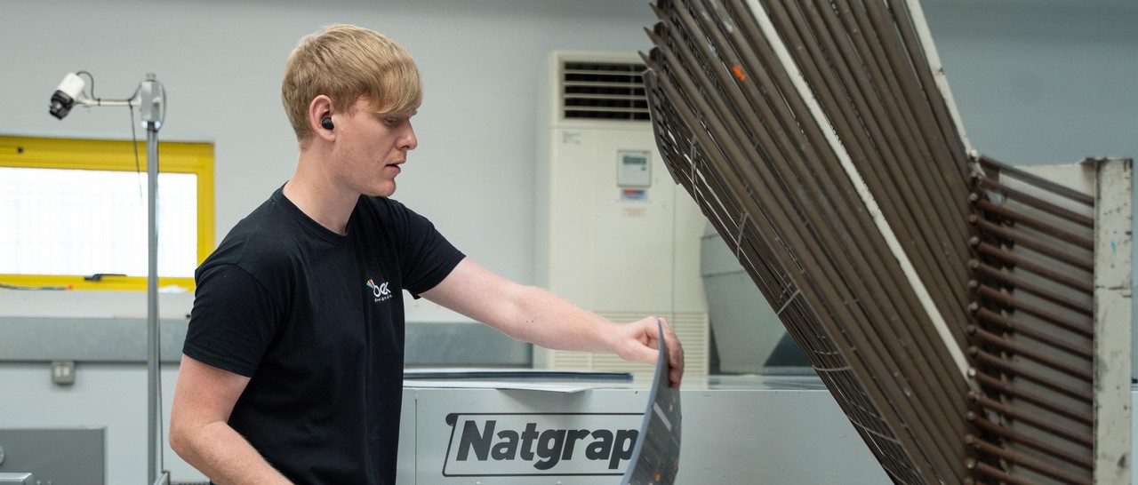 Bex specialist examining a piece of print equipment in a workshop setting.