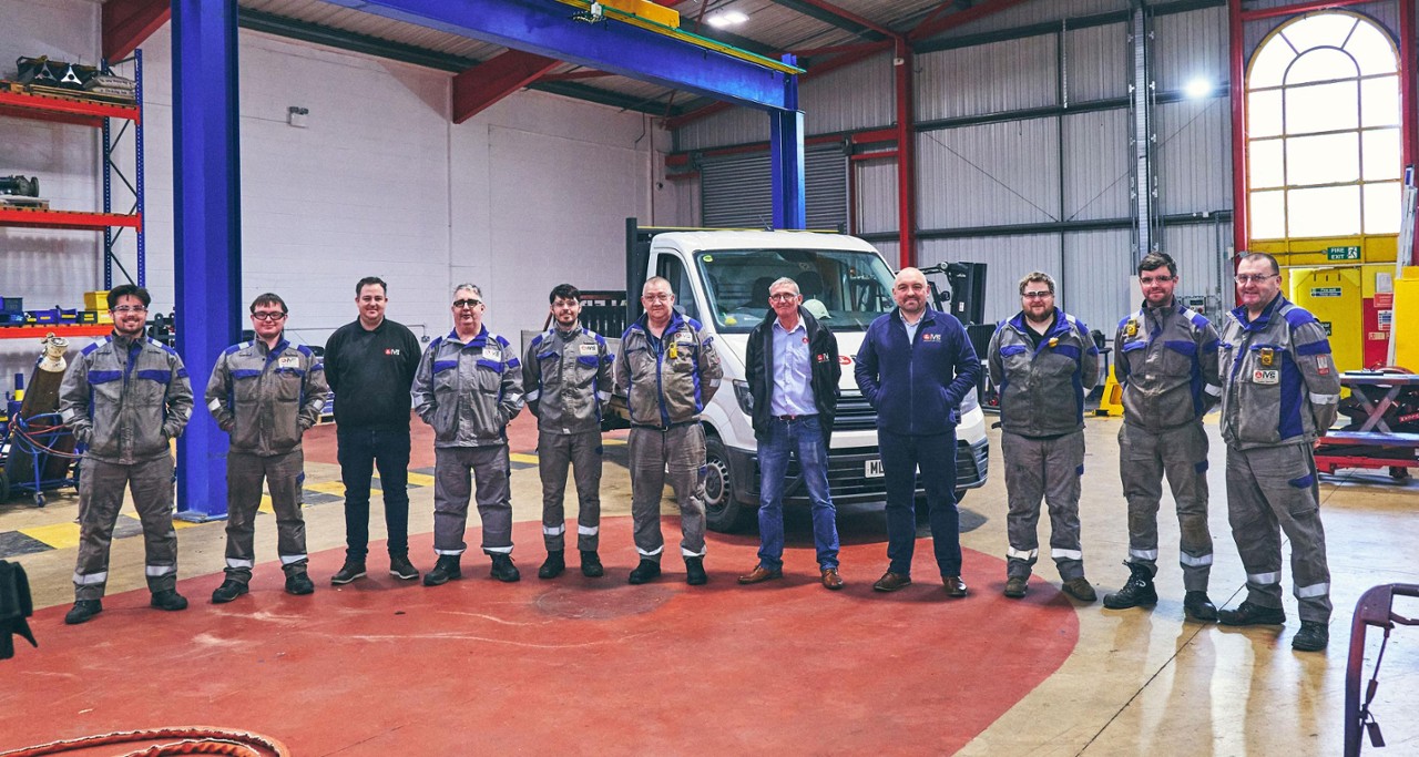 Amcomri Group Team - Group of IVS technicians posing in a well-equipped industrial maintenance workshop.