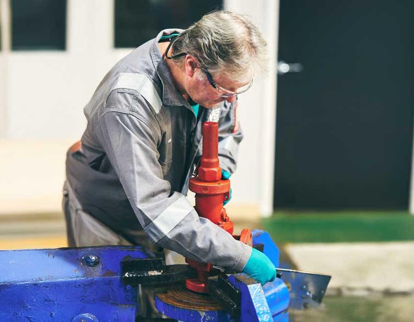 IVS worker wearing safety gear, adjusting a red industrial valve.