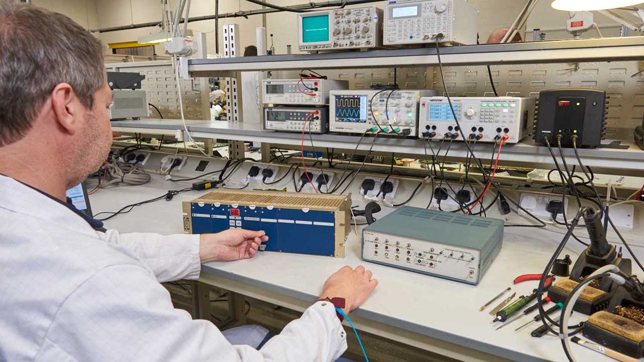 Technician testing and repairing electronic equipment in a well-equipped workshop.